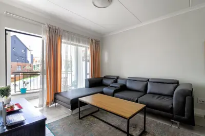 a living room with a black couch and a table at Lovely 2 bed @TheBlyde in Pretoria