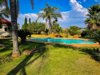 a swimming pool in a yard with palm trees at Bobisemo Lux Guesthouse in Tierpoort