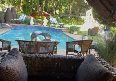 a swimming pool with wicker chairs and a swimming pool at The Presidential Suite at Frederick's Place in Pretoria