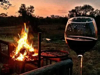 a glass of wine sitting next to a fire at Mokaikai - The Great Buffalo in Mabula