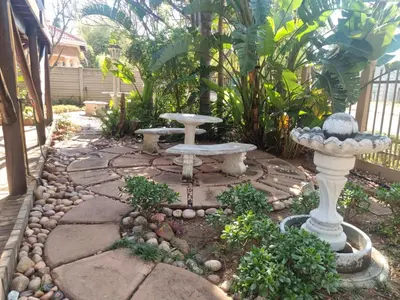 a garden with a stone walkway with a bird bath and a bench at Wooden Log House in Bela-Bela
