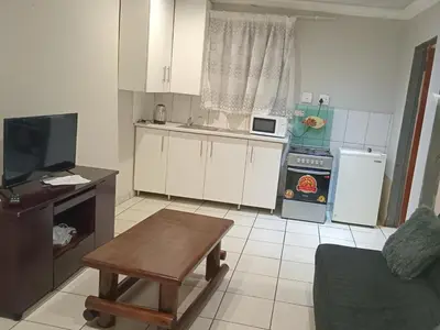 a kitchen with white cabinets and a table and a tv at Kama house in Pretoria