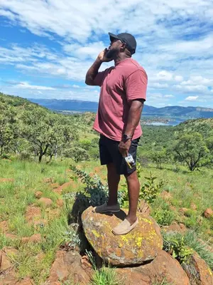 a man standing on a rock talking on a cell phone at Chalet 4 at Cynthias Country in Hartbeespoort