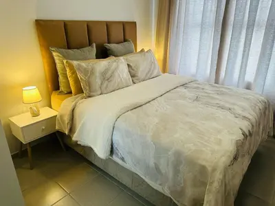 a bedroom with a large bed with a nightstand and a window at Calm & Cozy Apartment 3 in Pretoria