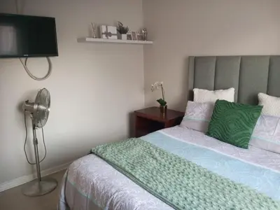 a bedroom with a bed with a green blanket and a fan at Urban Nest in Polokwane