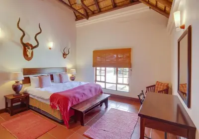 a bedroom with a bed and a desk and a window at Zebula 1 Pela Lodge, 6 bedrooms in Warmbaths