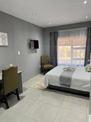 a bedroom with a bed and a desk and a window at Glowti Event & Guest House in Centurion
