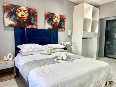 a bedroom with a large white bed with paintings on the wall at Glowti Event & Guest House in Centurion