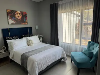 a bedroom with a bed and a chair and a window at Glow Events &Guest House in Centurion