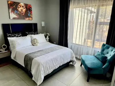 a bedroom with a large bed and a blue chair at Glow Events & Guest House in Centurion