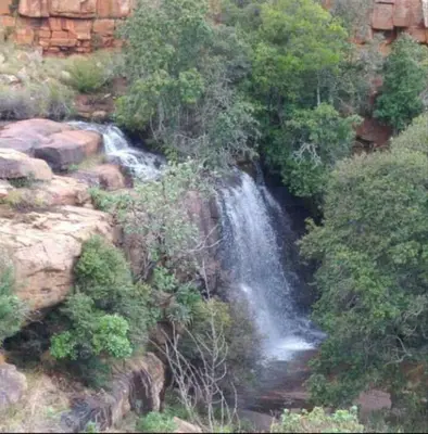 a waterfall on the side of a mountain with trees at AmaZeng chalet Wolf in Lydenburg