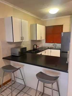 a kitchen with a black counter and two stools at Menlyn Place 512 in Pretoria