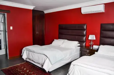 two beds in a room with a red wall at Casadeross Guest House in Pretoria