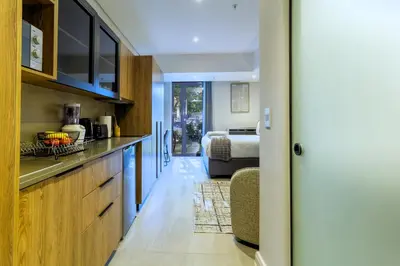 a kitchen with wooden cabinets and a bed in a room at #AlimamaSpaces Rob's Menlyn Maine in Pretoria