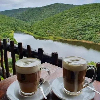 two cups of coffee sitting on a table overlooking a river at Mingwe Private Game Lodge in Mabula