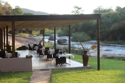 a pavilion with tables and chairs and a river at Lions Rock Rapids - Luxury Tented Camp in Hazyview