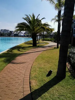 a walkway next to the water with palm trees at The Blyde Beach View in Pretoria